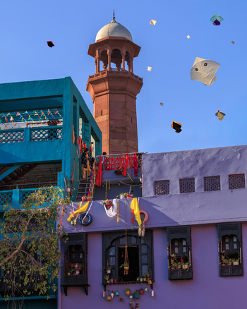 View of the historic minaret rising above colorful buildings adorned with festive decorations during the Basant kite festival in Lahore Punjab Pakistan.