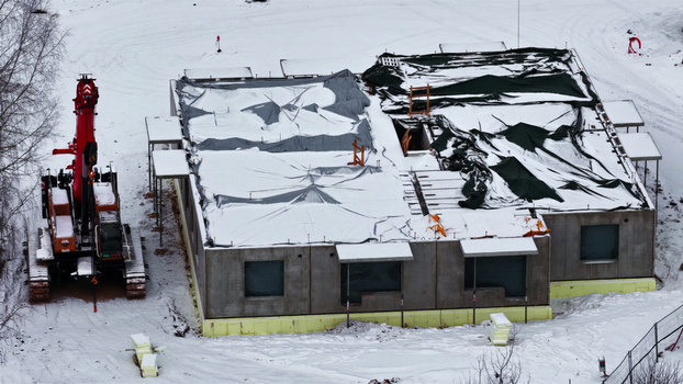 Aerial view of a construction site with a building covered in protective tarps and a red crane on a snow covered ground in Latvija. Aerial view of a construction site with a building covered in protective tarps and a red crane on a snow covered ground in Latvija.