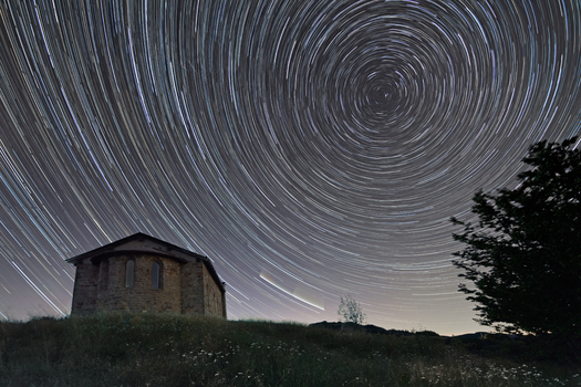View of the stone chapel at Passo di Cirone under a night sky with circular star trails and grassy foreground in Pontremoli Toscana Italy. View of the stone chapel at Passo di Cirone under a night sky with circular star trails and grassy foreground in Pontremoli Toscana Italy.