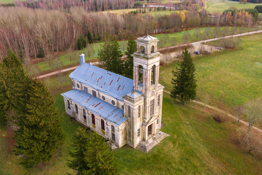 Aerial view of the historic Palendriai church with its tall bell tower and blue metal roof surrounded by autumn trees and green fields in Palendriai Siauliu apskritis Lithuania.