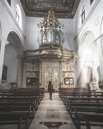 View of the ornate golden pipe organ and wooden pews inside a historic church with a woman standing in the aisle in Polignano a Mare Apulia Italy.