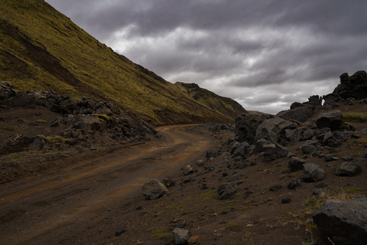 View of a winding dirt road cuts through the stark rocky landscape under a heavy moody sky Skaftárhreppur Skaftárhreppur Iceland. View of a winding dirt road cuts through the stark rocky landscape under a heavy moody sky Skaftárhreppur Skaftárhreppur Iceland.