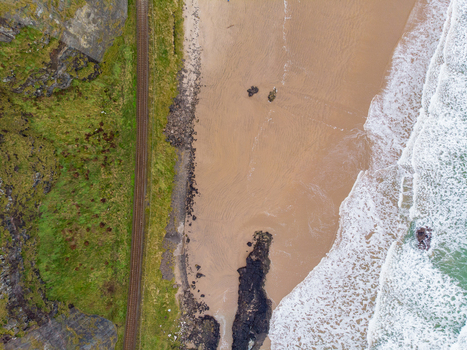Aerial view of Mussenden Temple perched on the cliff edge above a sandy beach with railway tracks running along the grassy coastline in Coleraine Northern Ireland United Kingdom. Aerial view of Mussenden Temple perched on the cliff edge above a sandy beach with railway tracks running along the grassy coastline in Coleraine Northern Ireland United Kingdom.