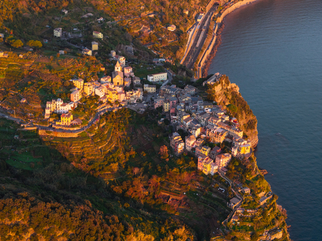 Aerial view of Corniglia village perched on a high cliff with colorful houses and terraced vineyards overlooking the sea at sunset Corniglia Liguria Italy. Aerial view of Corniglia village perched on a high cliff with colorful houses and terraced vineyards overlooking the sea at sunset Corniglia Liguria Italy.