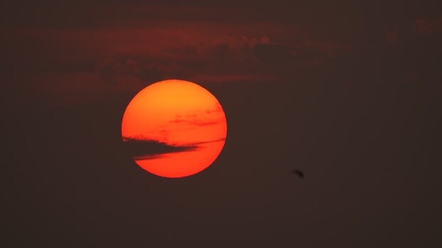 View of a large orange sun setting behind thin clouds Bangladesh. View of a large orange sun setting behind thin clouds Bangladesh.