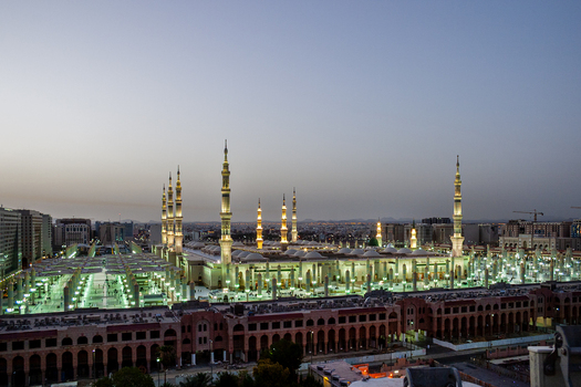 View of Al Masjid e Nabawi illuminated at dusk with its iconic minarets and expansive courtyard in Madinah Al Madinah Province Saudi Arabia.