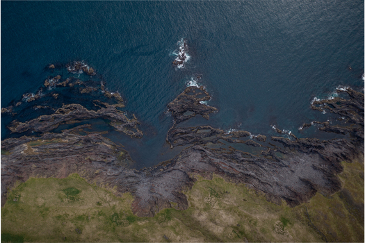 Aerial view of the dramatic volcanic coastline at Djupalonssandur featuring dark jagged rock formations meeting the deep blue ocean and green grassy cliffs in Iceland. Aerial view of the dramatic volcanic coastline at Djupalonssandur featuring dark jagged rock formations meeting the deep blue ocean and green grassy cliffs in Iceland.