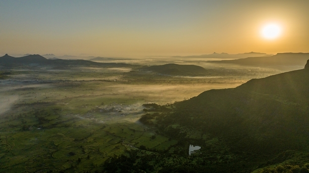 Aerial view of the misty valley in Igatpuri at sunrise featuring lush green fields rolling hills and golden morning light in Igatpuri Maharashtra India.