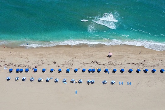 Aerial view of Singer Island beach featuring rows of blue and white umbrellas on the sand and turquoise ocean waves in Riviera Beach Florida United States. Aerial view of Singer Island beach featuring rows of blue and white umbrellas on the sand and turquoise ocean waves in Riviera Beach Florida United States.