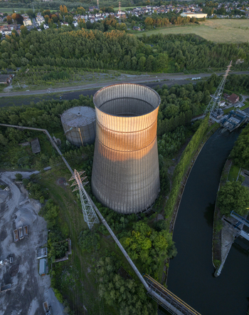 Aerial view of the abandoned Power Plant IM cooling tower surrounded by lush greenery and a canal in Charleroi Wallonia Belgium.