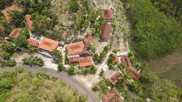 Aerial view of Baron Beach resort buildings with terracotta rooftops nestled among lush green trees and winding roads in Tanjungsari Special Region of Yogyakarta Indonesia. Aerial view of Baron Beach resort buildings with terracotta rooftops nestled among lush green trees and winding roads in Tanjungsari Special Region of Yogyakarta Indonesia.