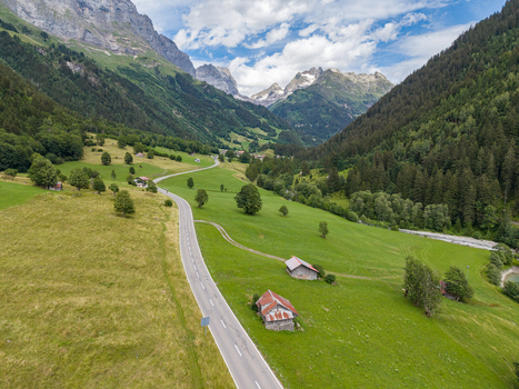 Aerial view of a winding road through the lush green valley of Gadmen surrounded by alpine mountains pine forests and traditional wooden huts in Gadmen Switzerland.