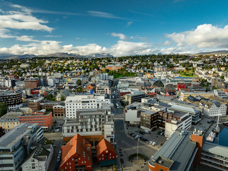 Aerial view of the city center featuring dense urban architecture colorful buildings harbor area and distant mountains under a blue sky in Tromso Troms Norway.