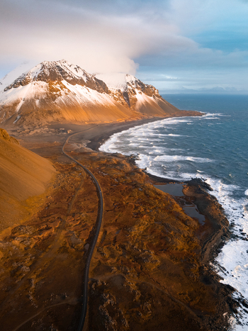 Aerial view of Hvalnes Lighthouse situated along the rugged coastline with snow capped mountains and a winding road in Hornafjordur Iceland. Aerial view of Hvalnes Lighthouse situated along the rugged coastline with snow capped mountains and a winding road in Hornafjordur Iceland.