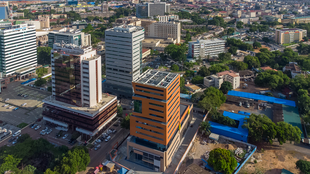 Accra Ghana 26 May 2023 Aerial view of modern office buildings and skyscrapers in the city center featuring a prominent orange tower urban infrastructure and lush trees. Accra Ghana 26 May 2023 Aerial view of modern office buildings and skyscrapers in the city center featuring a prominent orange tower urban infrastructure and lush trees.