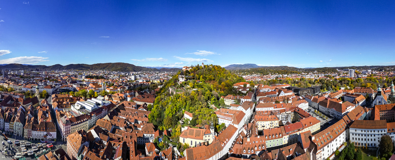 Aerial view of the vibrant red rooftops cascading towards the verdant Schlossberg hill crowned by the clock tower a timeless landmark Graz Styria Austria.