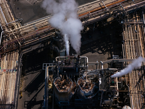 Aerial view of an industrial oil refinery complex with intricate piping networks storage tanks and steam venting from chimneys in Carson California United States.