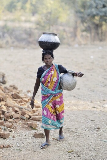 Odisha India 26 March 2026 View of a woman in a vibrant sari carrying water pots a testament to enduring traditions against a backdrop of earthy tones. Odisha India 26 March 2026 View of a woman in a vibrant sari carrying water pots a testament to enduring traditions against a backdrop of earthy tones.