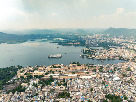 Aerial view of the City Palace complex situated on the banks of Lake Pichola with historic rooftops and surrounding urban landscape in Udaipur Rajasthan India. Aerial view of the City Palace complex situated on the banks of Lake Pichola with historic rooftops and surrounding urban landscape in Udaipur Rajasthan India.