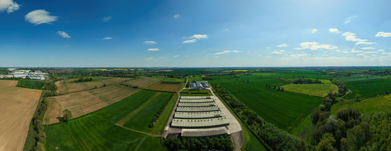 Aerial view of industrial agricultural buildings surrounded by vast green fields and lush trees under a clear blue sky Kettering England United Kingdom. Aerial view of industrial agricultural buildings surrounded by vast green fields and lush trees under a clear blue sky Kettering England United Kingdom.