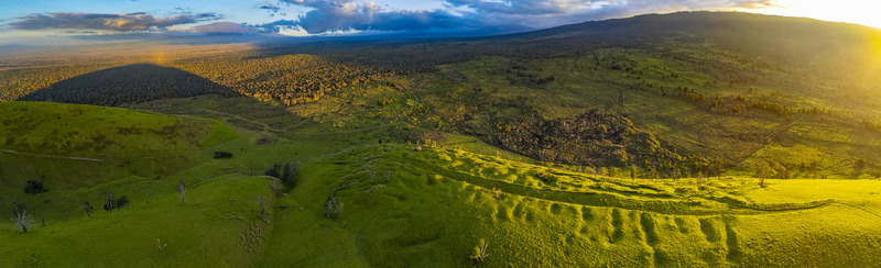 Aerial view of the Puu Waawaa cinder cone and lush green volcanic hills under a golden sunset light with dramatic shadows and distant lava fields Hawaii County Hawaii United States. Aerial view of the Puu Waawaa cinder cone and lush green volcanic hills under a golden sunset light with dramatic shadows and distant lava fields Hawaii County Hawaii United States.