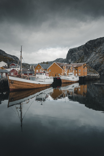 Nusfjord Nordland Norway 07 September 2022 View of traditional fishing boats moored at the historic harbor of Nusfjord with yellow rorbu cabins and rocky cliffs. Nusfjord Nordland Norway 07 September 2022 View of traditional fishing boats moored at the historic harbor of Nusfjord with yellow rorbu cabins and rocky cliffs.