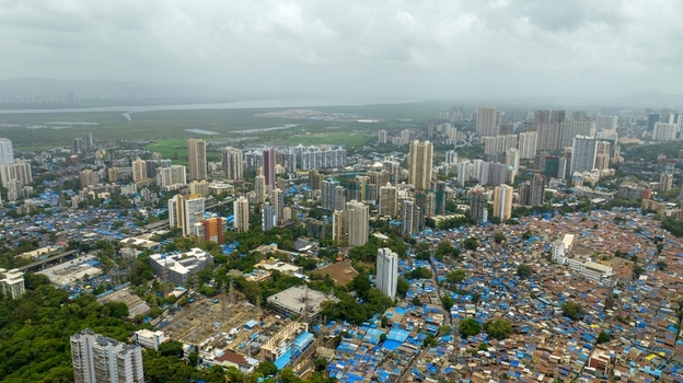 Aerial view of Dharavi Slums showing the contrast between dense informal settlements with blue tarpaulin roofs and modern high rise buildings in Mumbai Maharashtra India. Aerial view of Dharavi Slums showing the contrast between dense informal settlements with blue tarpaulin roofs and modern high rise buildings in Mumbai Maharashtra India.
