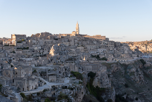 Aerial view of the historic Sassi di Matera with ancient stone dwellings narrow streets and the cathedral bell tower illuminated by golden hour light in Matera Basilicata Italy.