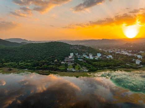 Aerial view of a serene lake surrounded by lush green hills and buildings in Udaipur Rajasthan India.