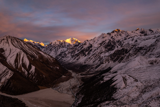 Aerial view of snow capped Himalayan peaks illuminated by the golden light of sunset above a rugged valley in Nepal.