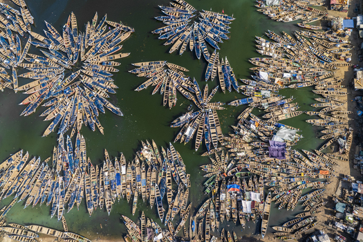 Aerial view of wooden boats clustered like petals on the water s surface creating floral patterns of brown against the dark green Tema Ghana. Aerial view of wooden boats clustered like petals on the water s surface creating floral patterns of brown against the dark green Tema Ghana.