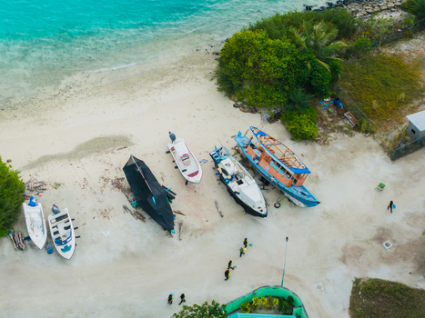 Aerial view of boats resting on the sandy shore next to turquoise waters and lush greenery Vashafaru Island Maldives. Aerial view of boats resting on the sandy shore next to turquoise waters and lush greenery Vashafaru Island Maldives.