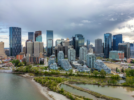 Aerial view of the Calgary skyline featuring modern skyscrapers glass office towers and residential buildings along the Bow River under a cloudy sky in Calgary Alberta Canada.