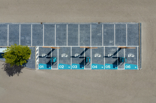 Aerial view of an electric vehicle charging station with numbered parking spots in a parking lot featuring a green tree on the left in Beilen Drenthe Netherlands.