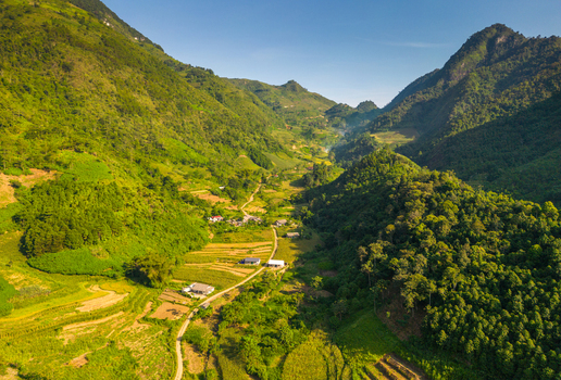 Aerial view of a lush green valley with terraced fields small rural houses and winding dirt paths nestled between steep mountains in Quan Ba Tuyen Quang Vietnam.