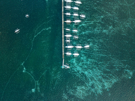 Aerial view of a long wooden pier with traditional outrigger boats docked in the clear turquoise waters surrounding Naked Island Siargao Philippines. Aerial view of a long wooden pier with traditional outrigger boats docked in the clear turquoise waters surrounding Naked Island Siargao Philippines.