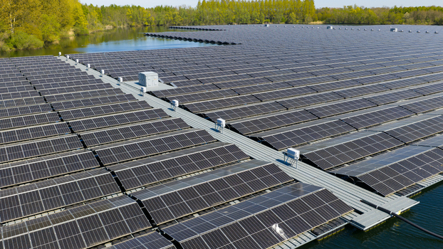 Aerial view of a large floating solar farm with rows of photovoltaic panels on a calm lake surrounded by green trees in Zwolle Overijssel Netherlands. Aerial view of a large floating solar farm with rows of photovoltaic panels on a calm lake surrounded by green trees in Zwolle Overijssel Netherlands.