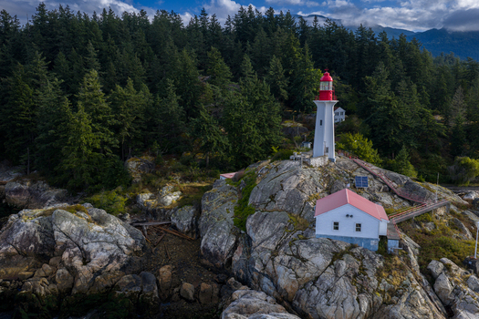 Aerial view of Point Atkinson Lighthouse with its red lantern atop a white tower set on rugged rocky cliffs amidst a dense evergreen forest in West Vancouver British Columbia Canada.