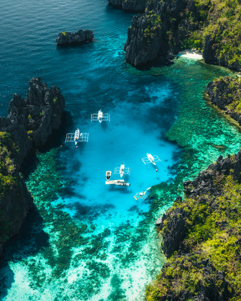 Aerial view of Big Lagoon with turquoise waters limestone cliffs and outrigger boats in El Nido Bay Philippines. Aerial view of Big Lagoon with turquoise waters limestone cliffs and outrigger boats in El Nido Bay Philippines.
