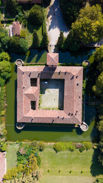 Aerial view of Castello di Peschiera Borromeo with its square structure and terracotta roof tiles surrounded by a moat and lush green trees in Peschiera Borromeo Lombardy Italy.