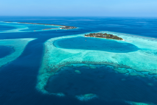 Aerial view of the tropical island of Vaanee surrounded by vibrant turquoise lagoon waters coral reefs and deep blue ocean in Vaanee Dhaalu Atoll Maldives. Aerial view of the tropical island of Vaanee surrounded by vibrant turquoise lagoon waters coral reefs and deep blue ocean in Vaanee Dhaalu Atoll Maldives.