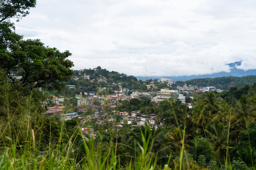 View of the urban landscape nestled among lush green hills and tropical trees under a cloudy sky in Kandy Central Province Sri Lanka. View of the urban landscape nestled among lush green hills and tropical trees under a cloudy sky in Kandy Central Province Sri Lanka.