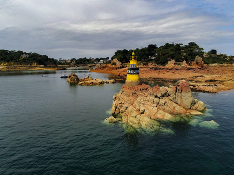 Aerial view of the yellow Paon lighthouse perched on a rocky outcrop surrounded by calm sea waters off the coast of Ile de Brehat Brittany France.