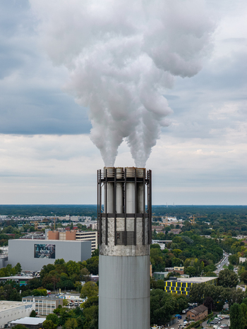 Aerial view of the industrial chimney at Klarwerk Ruhleben with thick white steam rising into the cloudy sky above the urban landscape of Berlin Berlin Germany.