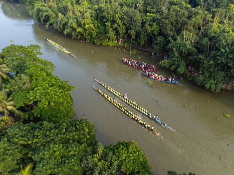Aerial view of boats racing down a winding river flanked by lush green trees showcasing a vibrant display of tradition and nature Gopalganj Bangladesh. Aerial view of boats racing down a winding river flanked by lush green trees showcasing a vibrant display of tradition and nature Gopalganj Bangladesh.