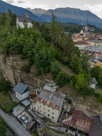 Aerial view of historic houses built into the cliffside with a church on the hill and the town of Imst in the background Imst Tyrol Austria.