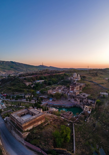 Aerial view of Katas Raj Temple Complex featuring ancient stone structures and a sacred pond surrounded by arid hills at sunset in Katas Punjab Pakistan. Aerial view of Katas Raj Temple Complex featuring ancient stone structures and a sacred pond surrounded by arid hills at sunset in Katas Punjab Pakistan.