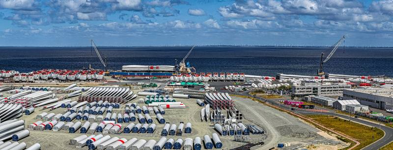 Aerial view of Siemens Gamesa Renewable Energy wind turbine blade storage facility at the port with cranes industrial components and cargo ship in Cuxhaven Niedersachsen Germany.