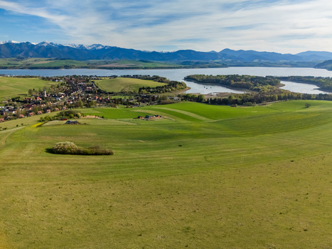 Aerial view of Liptovsky Trnovec village with rolling green fields Liptovska Mara lake and snow capped Tatra Mountains in the background Liptovsky Trnovec Zilina Region Slovakia.