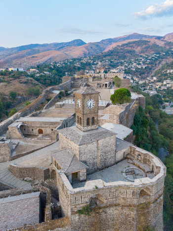 Aerial view of Gjirokaster Fortress with its iconic clock tower stone walls and surrounding historic town nestled in the mountains in Gjirokaster Gjirokaster County Albania. Aerial view of Gjirokaster Fortress with its iconic clock tower stone walls and surrounding historic town nestled in the mountains in Gjirokaster Gjirokaster County Albania.